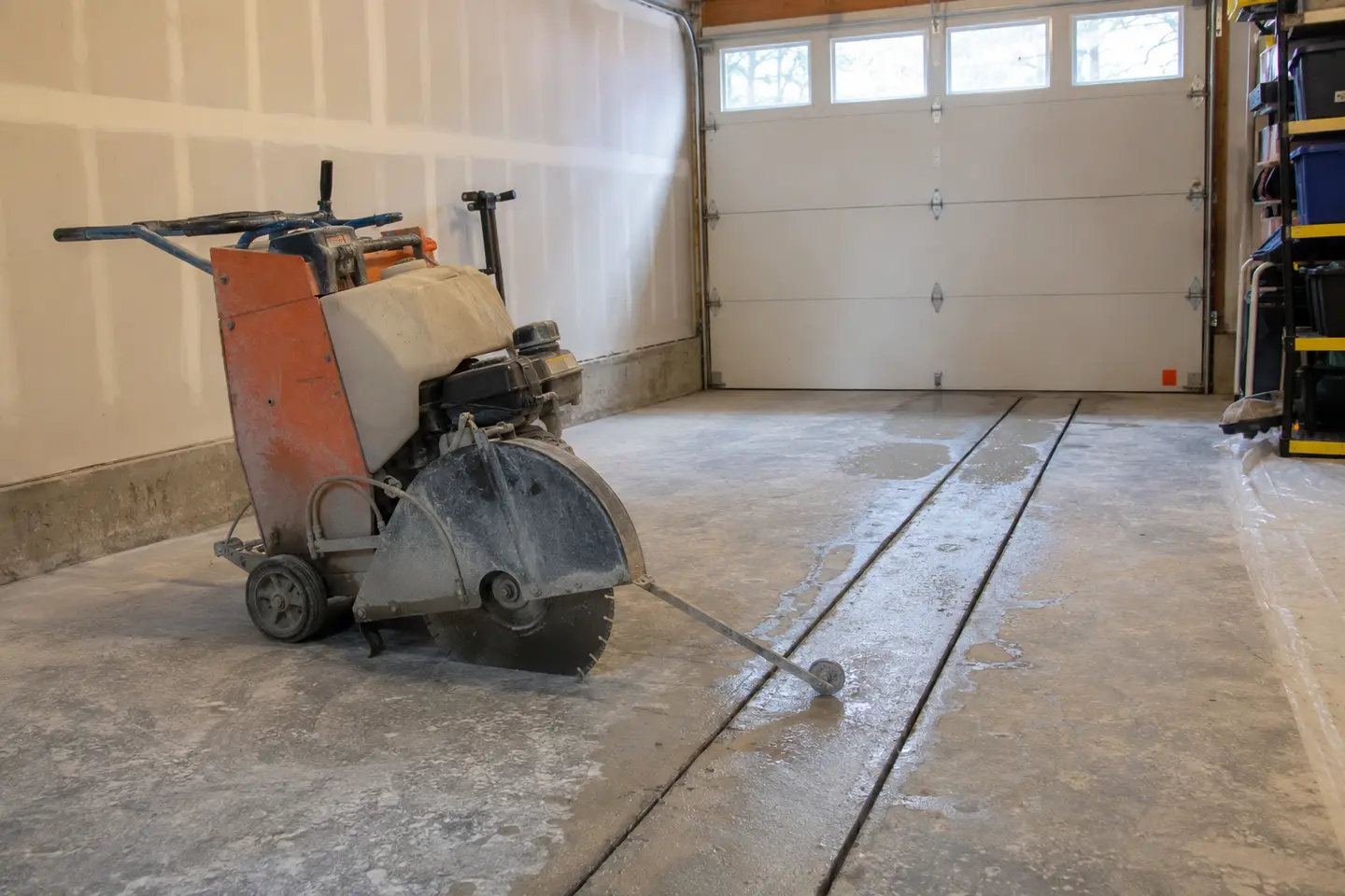 Walk-behind diamond slab saw parked beside fresh parallel floor cuts in an attached residential garage in Edmonton