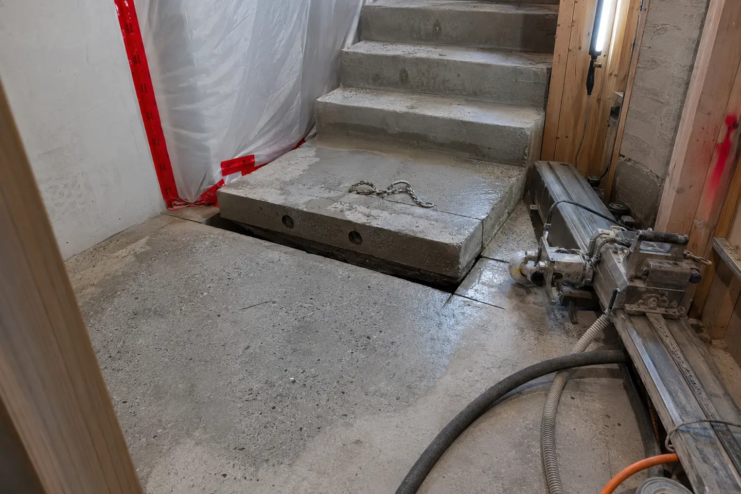 Precision concrete stair-landing modification with inactive rail saw equipment inside a residential basement stairwell